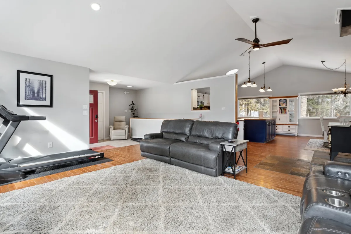 A welcoming open-plan space that blends a comfortable leather sofa, exercise treadmill, and large windows with views, as well as an open kitchen area. The arrangement encourages both relaxation and socializing, while the natural light enhances the inviting mood.