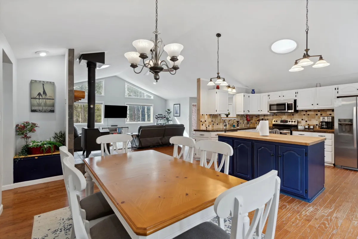 A warm, inviting dining area adjoins the kitchen, featuring a substantial dining table, an elegant chandelier, and a cozy fireplace. Large windows fill the space with natural light, creating a setting ideal for both intimate dinners and family gatherings. The overall ambiance is comfortable and welcoming, encouraging connection over shared meals.