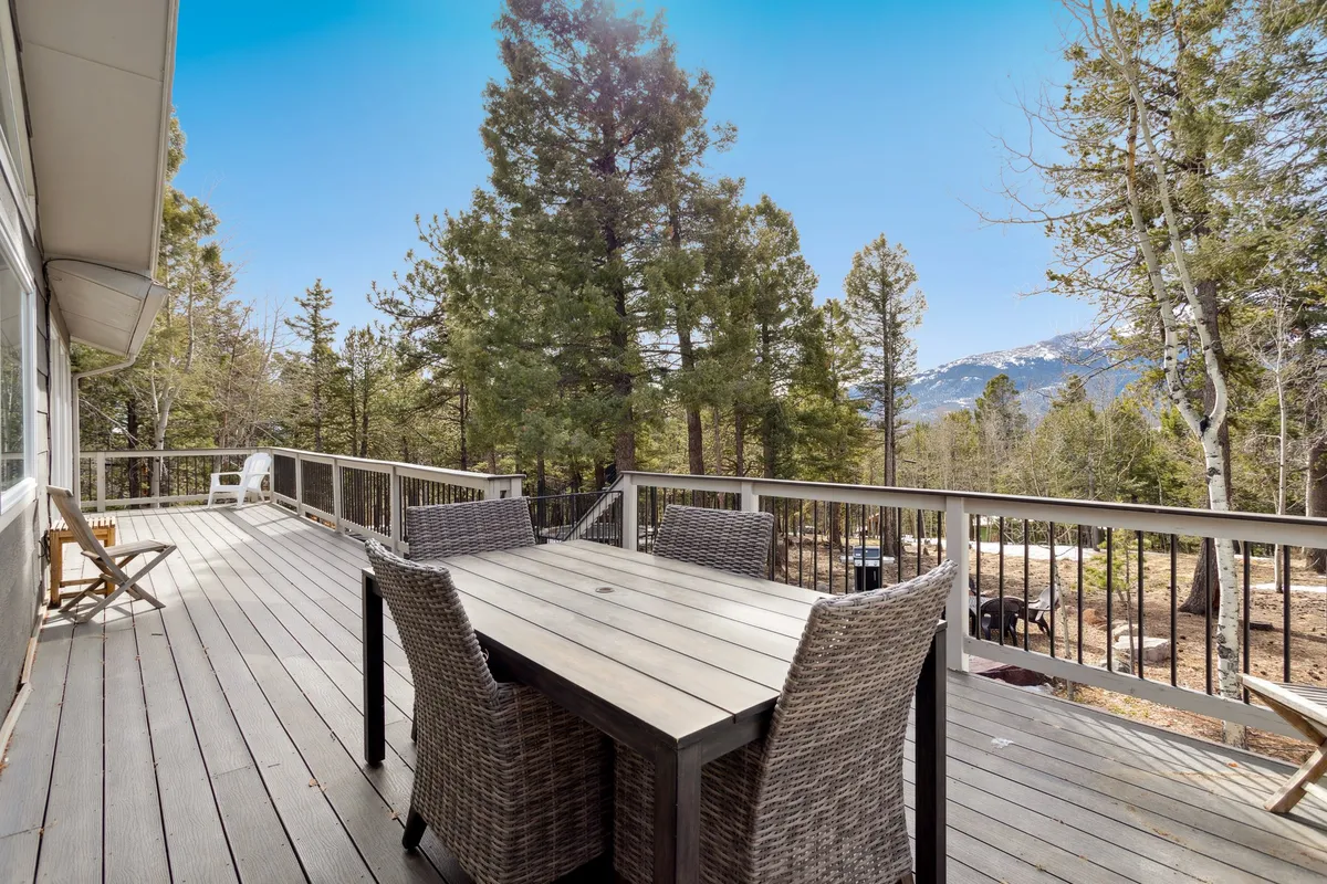 This image shows an outdoor dining table set amidst a tranquil pine forest, with a beautiful mountain view in the background. The table is positioned to take full advantage of the natural surroundings, providing an inviting space to dine, work, or relax outdoors. Tall evergreen trees frame the scene, emphasizing the connection to nature and the sense of peaceful seclusion.