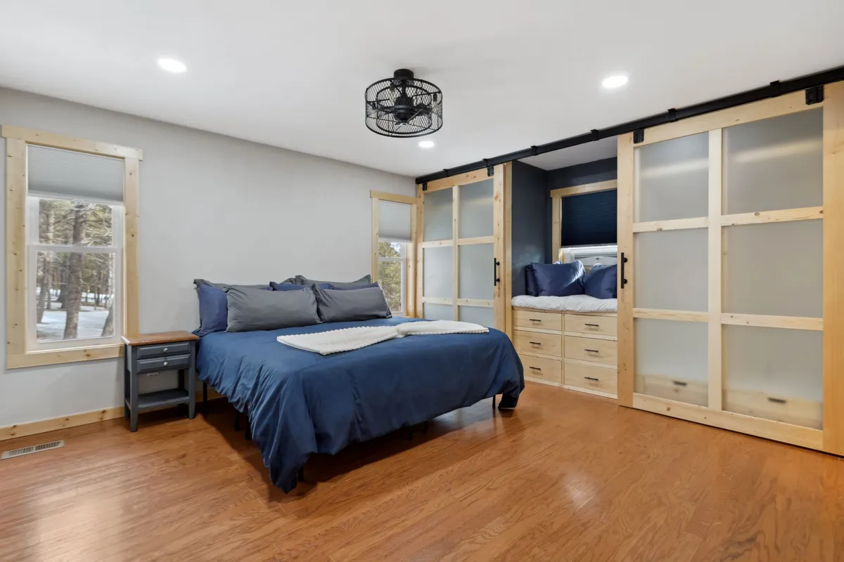 A tranquil bedroom featuring a bed with soft blue bedding, sliding glass doors allowing in natural light, and a wooden nightstand beside the bed. The gentle illumination and uncluttered décor evoke a sense of calm and comfort, perfect for unwinding after a long day.