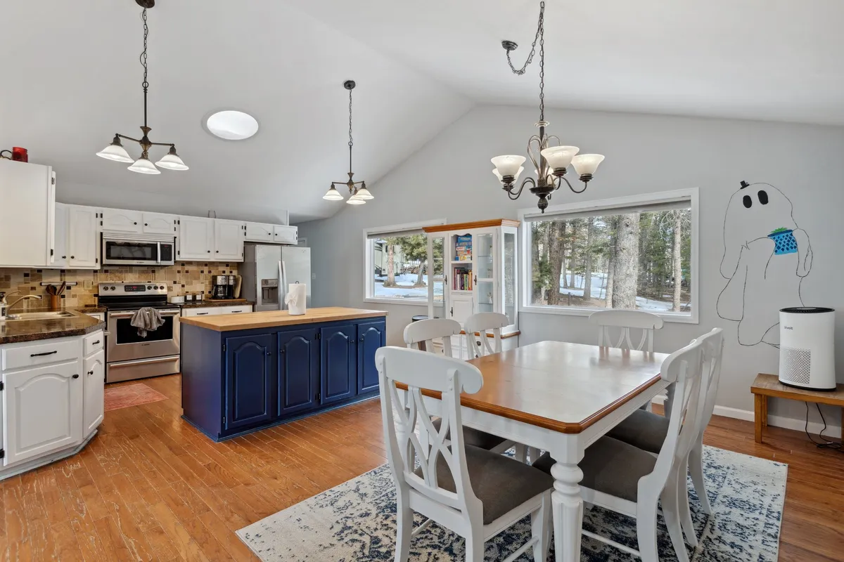 A cheerful open-concept kitchen and dining area with a kitchen island, dining table, large windows, and a unique ghost mural. The space is designed for both cooking and entertaining, with ample light streaming in and playful artistic touches that add character. The configuration encourages interaction and shared activities.