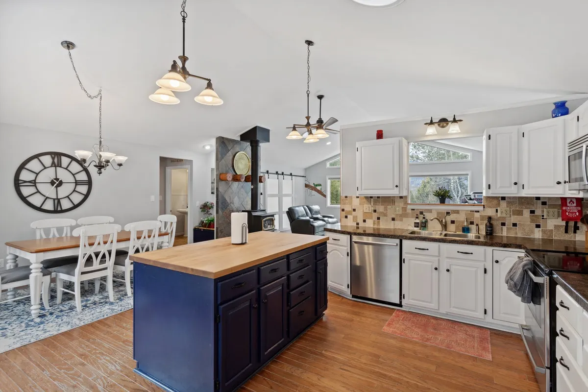 A bright dining nook adjacent to the kitchen, featuring a wooden dining table, blue cabinetry, and a large clock on the wall. The area is bathed in natural light from nearby windows, creating a cozy setting for meals and memorable family gatherings.